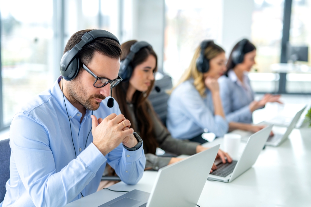 Pensive male customer service operator listening to customer over headset and thinking about appropriate solutions for client issues